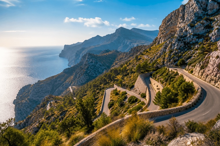 Vista panorámica de la Serra de Tramuntana en Mallorca con una carretera de montaña serpenteante entre acantilados, vegetación mediterránea y vistas al mar.